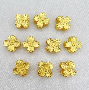 Close-up of ten gold hollow clover spacers with matte texture for jewelry making