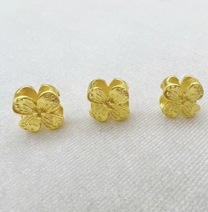Detailed macro view of three gold-plated hollow clover charms with a brushed metal finish