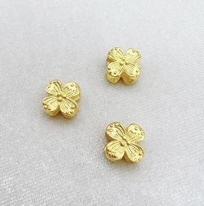 Detailed macro view of gold hollow four-leaf clover spacers with frosted texture finish