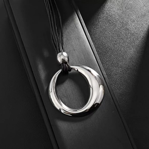 Close-up of polished irregular metal circle pendant with black layered cord strings