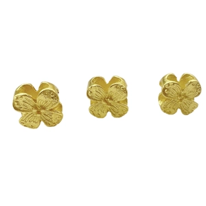 Three matte gold four-leaf clover pendant beads with textured petals on white background