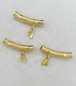 Detailed view of three gold bamboo-shaped curved tubes with leaf pendants for DIY jewelry