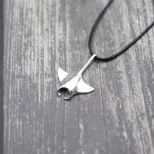 Polished silver manta ray pendant on black woven cord with a purple wood backdrop