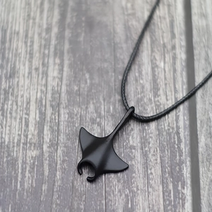 Punk manta ray pendant necklace with black matte finish on a leather cord over wood