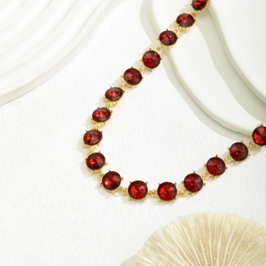 Detail van geometrische rode kristallen ketting met gouden zetting op witte achtergrond