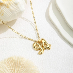 Close-up of golden number 94 balloon pendant on a classic Figaro chain necklace
