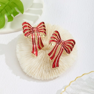 Close-up of sparkling red bow earrings with gold edges on a white textured base