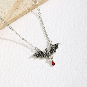 Detail of Gothic bat pendant with red resin teardrop gemstone on textured background