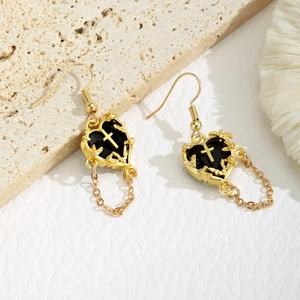 Boucles d'oreilles cœur gothiques dorées avec croix en relief et chaînes sur fond de pierre