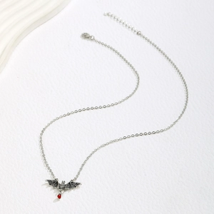 Detailed close-up of a silver bat pendant necklace with a red resin gemstone drop