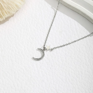 Close-up van zilveren maanhanger met kristallen en ster op witte textuurachtergrond