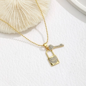 Detail van gouden ball chain ketting met een met diamant bezette slot en sleutel hanger