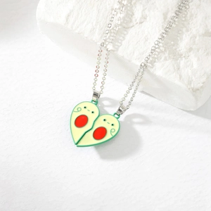 Detail of couple avocado magnetic heart necklaces with green enamel on a stone texture