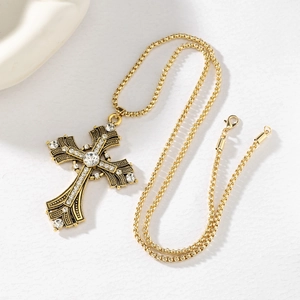 Close-up of golden cross necklace with white rhinestones and ornate baroque textures