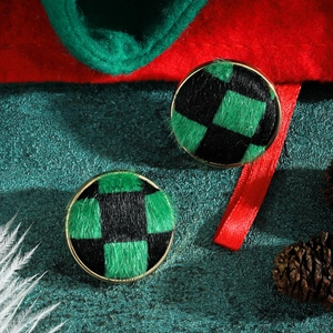 Close-up of circular checkered stud earrings with green velvet texture and gold edges