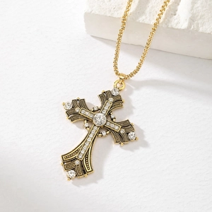 Macro shot of vintage gold cross necklace featuring intricate carvings and clear rhinestones