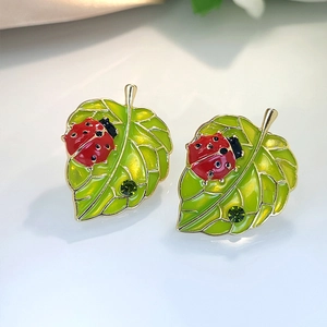Detailopname van lieveheersbeestje- en blad-oorbellen met emaille details en groen kristal