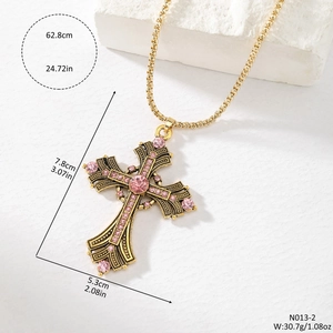 Detail of vintage gold cross pendant with pink rhinestones and embossed metal texture