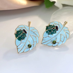 Macro-opname van blauwe emaille blad oorbellen met groen lieveheersbeestje goud