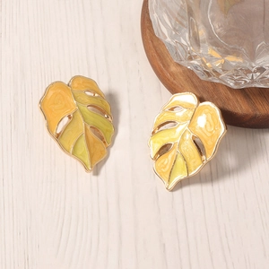 Gouden monstera-oorbellen met groen emaillegradiënt op een lichte houten tafel