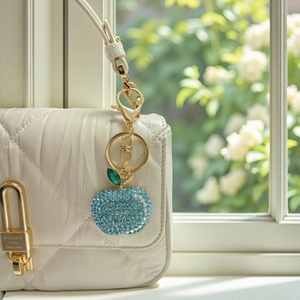 Detailed view of light blue rhinestone apple keychain attached to a white quilted handbag