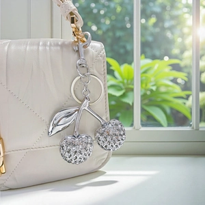 Sparkling crystal cherry keychain charm attached to a luxury quilted beige handbag
