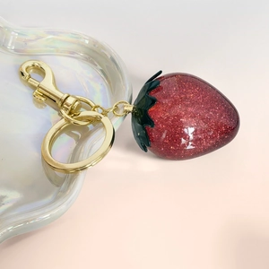 Detailed macro of a red resin strawberry keychain with golden glitter and lobster clasp