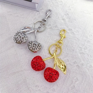 Close-up of sparkling crystal cherry keychains in gold and silver with metal leaves