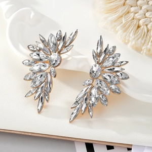 Macro detail of gold wing stud earrings with crystal rhinestones on a white ceramic tray