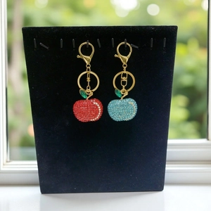 Detail of red and blue sparkling apple keychains with gold lobster clasp on velvet stand