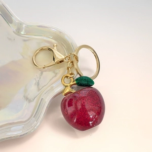 Macro shot of glitter red apple keychain with golden hardware on an iridescent tray
