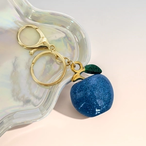 Detailed close-up of dark blue glitter apple keychain with golden lobster clasp and leaf