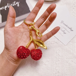 Close-up of sparkling rhinestone cherry keychain with gold stem held by hand