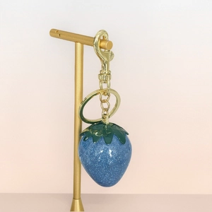 Sparkly blue strawberry keychain with gold lobster clasp and green leaves on display