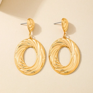 Close-up of golden oval drop earrings featuring spiral texture and polished metal finish