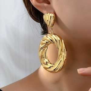 Close-up of model wearing chunky twisted gold hoop earrings with polished metal texture