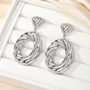 Chic silver twisted oval hoop earrings with heart stud on luxury white leather and silk background