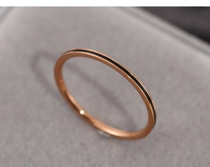 Macro view of a thin rose gold ring with a black enamel line inlay on a grey velvet box