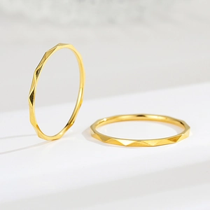 Detailed view of two rose gold V-shaped geometric faceted rings on a white pedestal