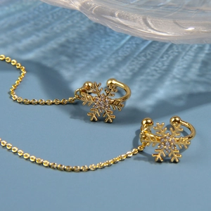 Détail du bijou d'oreille flocon doré avec zircon et chaîne sur fond texturé bleu