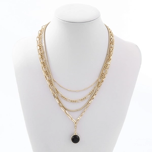 Detail of a gold multilayered necklace with snake chains and a black round pendant