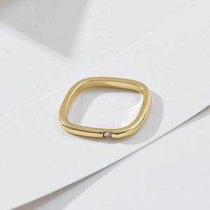 Minimalist gold square ring with a single zircon on geometric layered background