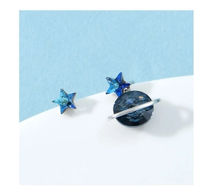 Detail view of asymmetric silver earrings featuring blue star and planet crystal charms