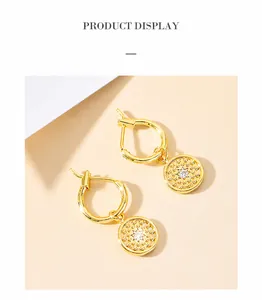 Close-up of gold starburst coin drop earrings with central cubic zirconia on beige background