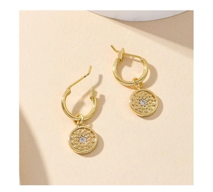 Detailed view of gold hoop earring featuring a starburst texture and central white zircon