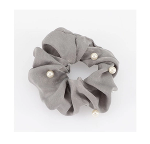 Détail d'un chouchou en satin gris foncé orné de perles blanches sur fond blanc neutre