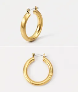 Détail macro de boucles d'oreilles créoles dorées en C avec finition mate brossée