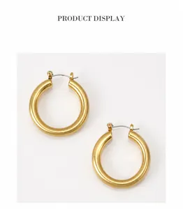 Détail de boucles d'oreilles créoles dorées avec finition mate brossée et fermoir à charnière