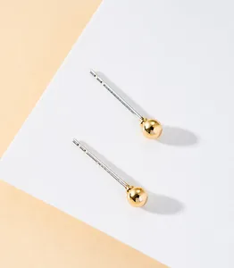 Close-up of minimalist geometric gold ball stud earrings on a sleek white display card