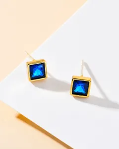 Detailed close-up of square stud earrings with blue faceted crystals and golden metal